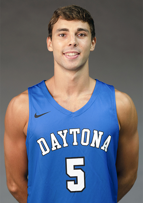 La imagen muestra a Javier Rodríguez con una camiseta de baloncesto azul. La camiseta tiene la palabra "Daytona" escrita en letras blancas en el pecho y el número 5 en el centro. El joven tiene el cabello corto y castaño, y está sonriendo. El fondo de la imagen es de color gris neutro.