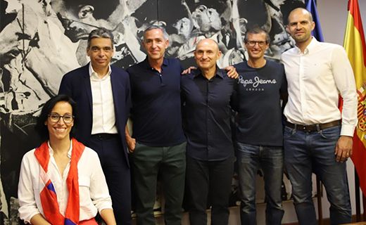 La imagen muestra a un grupo de seis personas posando para una foto. Cinco de ellos están de pie y una persona está sentada al frente. Detrás de ellos hay una bandera de España y un mural en blanco y negro. La URL en la barra de direcciones sugiere que la imagen está relacionada con un acuerdo del Consejo Superior de Deportes (CSD) de España.